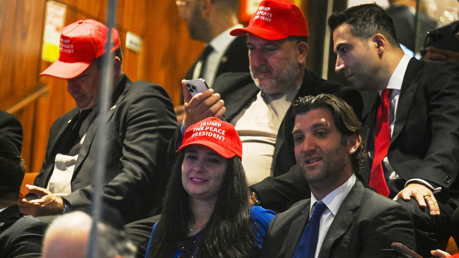 Menschen sitzen im israelischen Parlament und warten auf den US-Präsidenten. Sie tragen dabei rote Kappen mit der Aufschrift "Trump der Friedenspräsident"